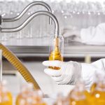 Production process of cosmetics in laboratory. Laboratory scientist dressed in hospital gown and gloves working at lab holding glassware with yellow liquid. Laboratory,scientific research concept.